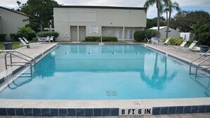 Una piscina rectangular con una profundidad de 1,8 metros, rodeada de sillas de descanso y un edificio con un letrero.