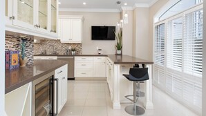 A modern kitchen with white cabinets, a tiled backsplash, a flat-screen TV, and a bar area with stools. - Spacious & Modern Home in The Heart of Toronto (Toronto)