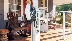 Une véranda en bois équipée d’une borne de recharge pour véhicules Tesla, d’une chaise berçante et d’une vieille roue de charrette.