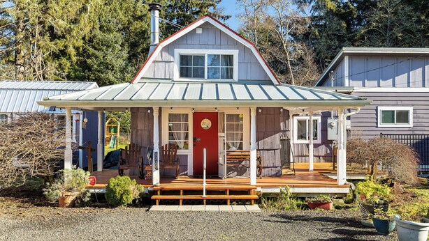Une cabane en bois avec une porte rouge, une véranda couverte et une petite terrasse.