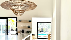 Una cucina moderna con un'isola grande, sgabelli di legno e un lampadario intrecciato originale.