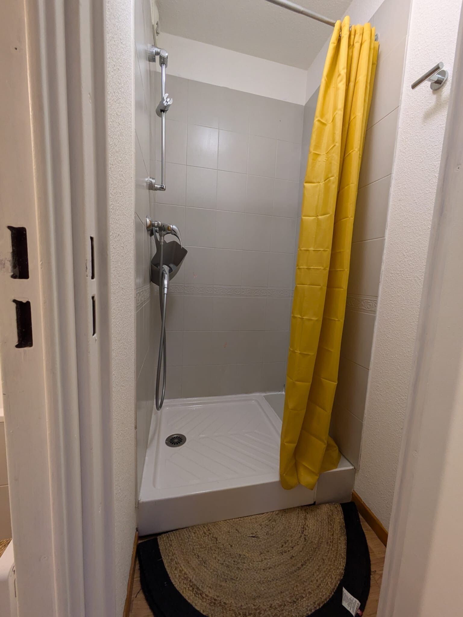 A shower area with a yellow shower curtain, a handheld showerhead, and a wall-mounted faucet.