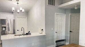 A modern kitchen with a stainless steel refrigerator, a white countertop, and a wooden dining table.