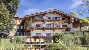A multi-story hotel with balconies, a pond in the foreground, and a clear blue sky. - Ferienwohnung mit 1 Schlafzimmer fur 6 Personen (Reith bei Kitzbuehel)