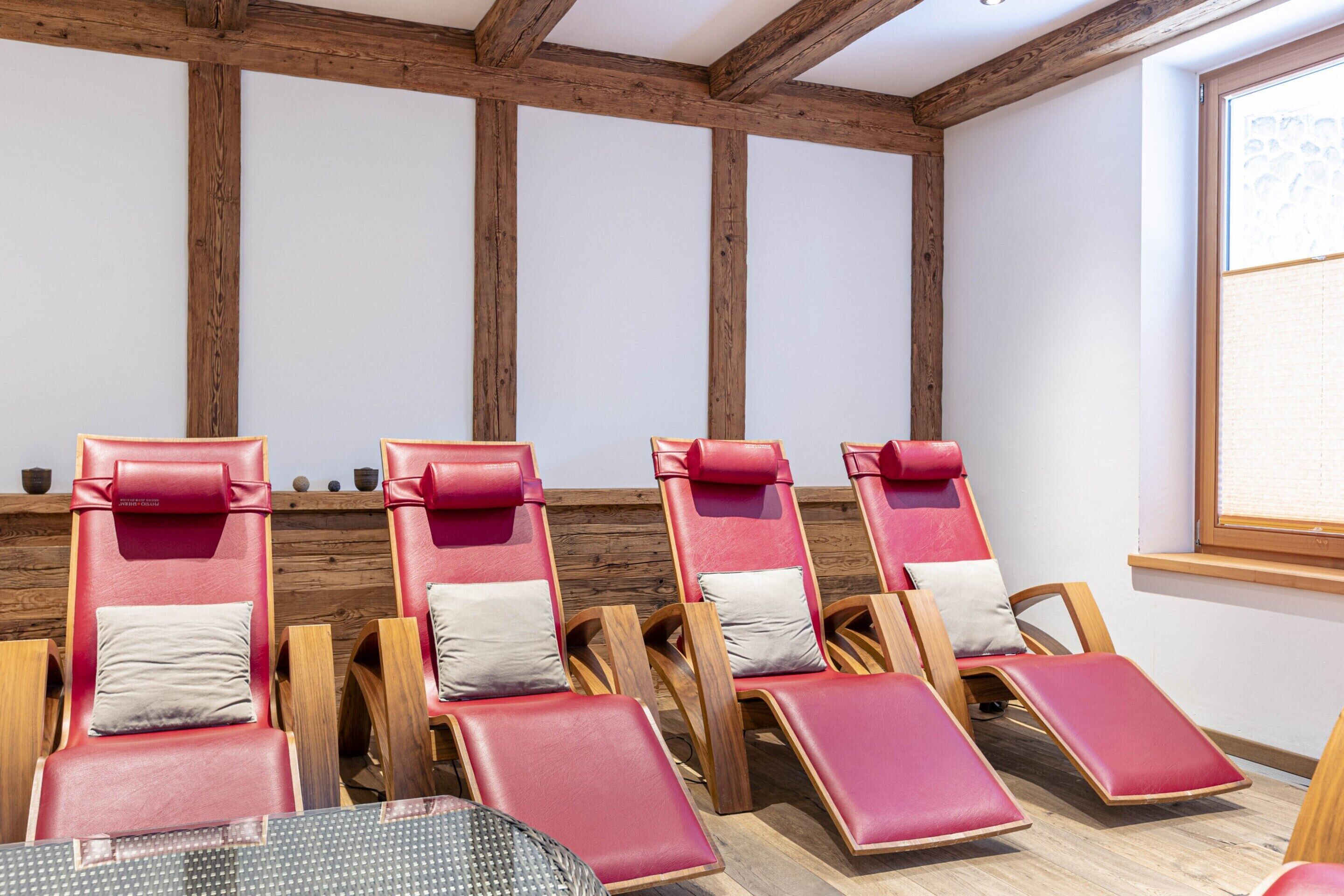 Una habitación con vigas de madera, sillones rojos con cojines blancos y una ventana con persianas.