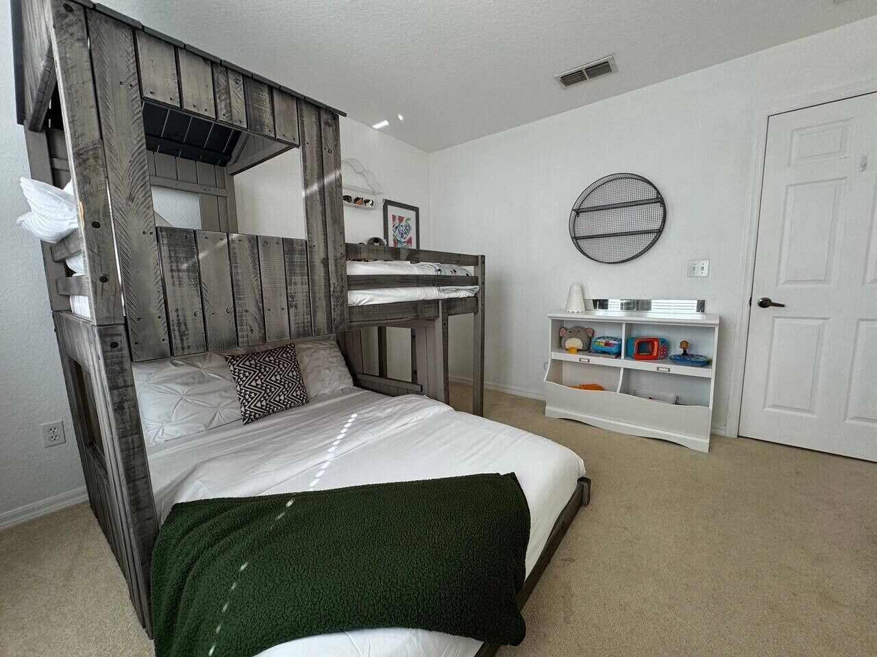 A bedroom with a wooden canopy bed, a white wall, a round mirror, and a white door.