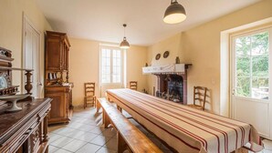 A dining area with a long table, benches, wooden cabinets, and a fireplace. - Charming cottage (Aldudes)