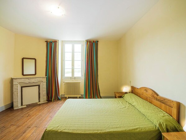 A bedroom with a bed, a nightstand, a fireplace, and a window with curtains.