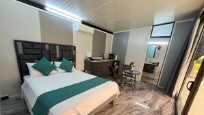Quarto de hotel com cama, escrivaninha, cadeira, mesa pequena e espelho.
