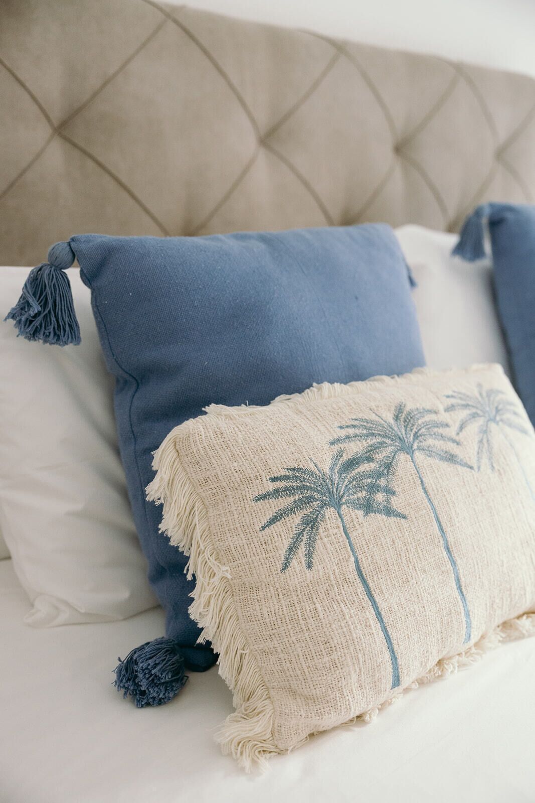 Una cama con cabecera capitonada, dos almohadas y un plaid decorativo.