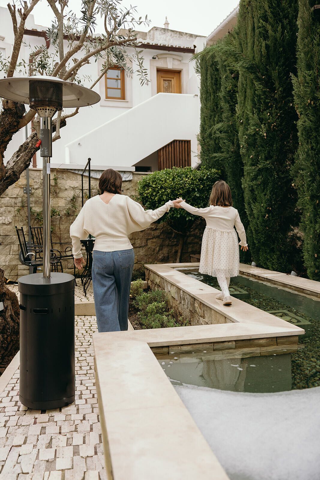 A courtyard with a stone pathway, a water feature, and a tall evergreen tree.