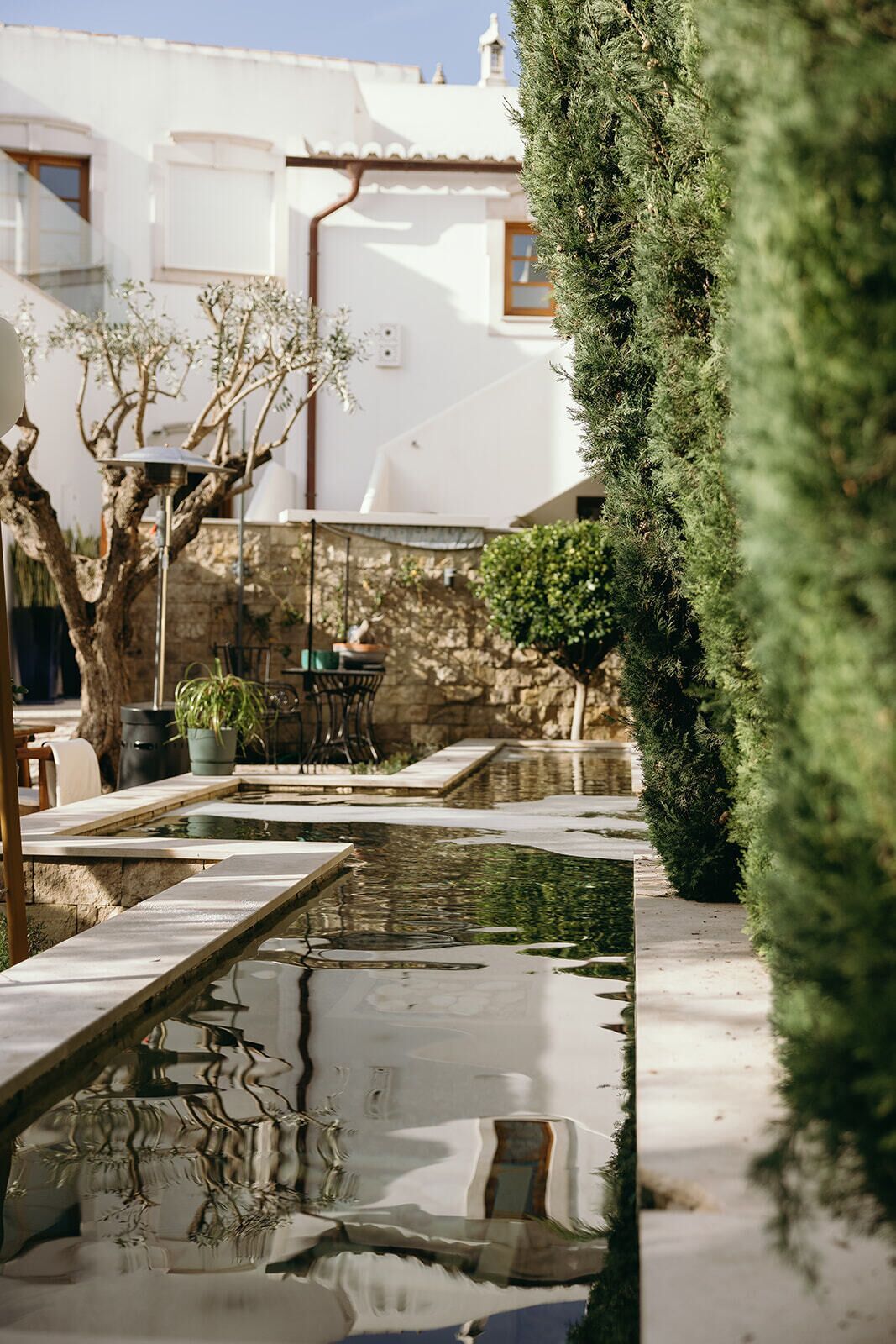 Un patio tranquilo con un pequeño estanque, un sendero de piedra y un edificio blanco con tejado de baldosas.