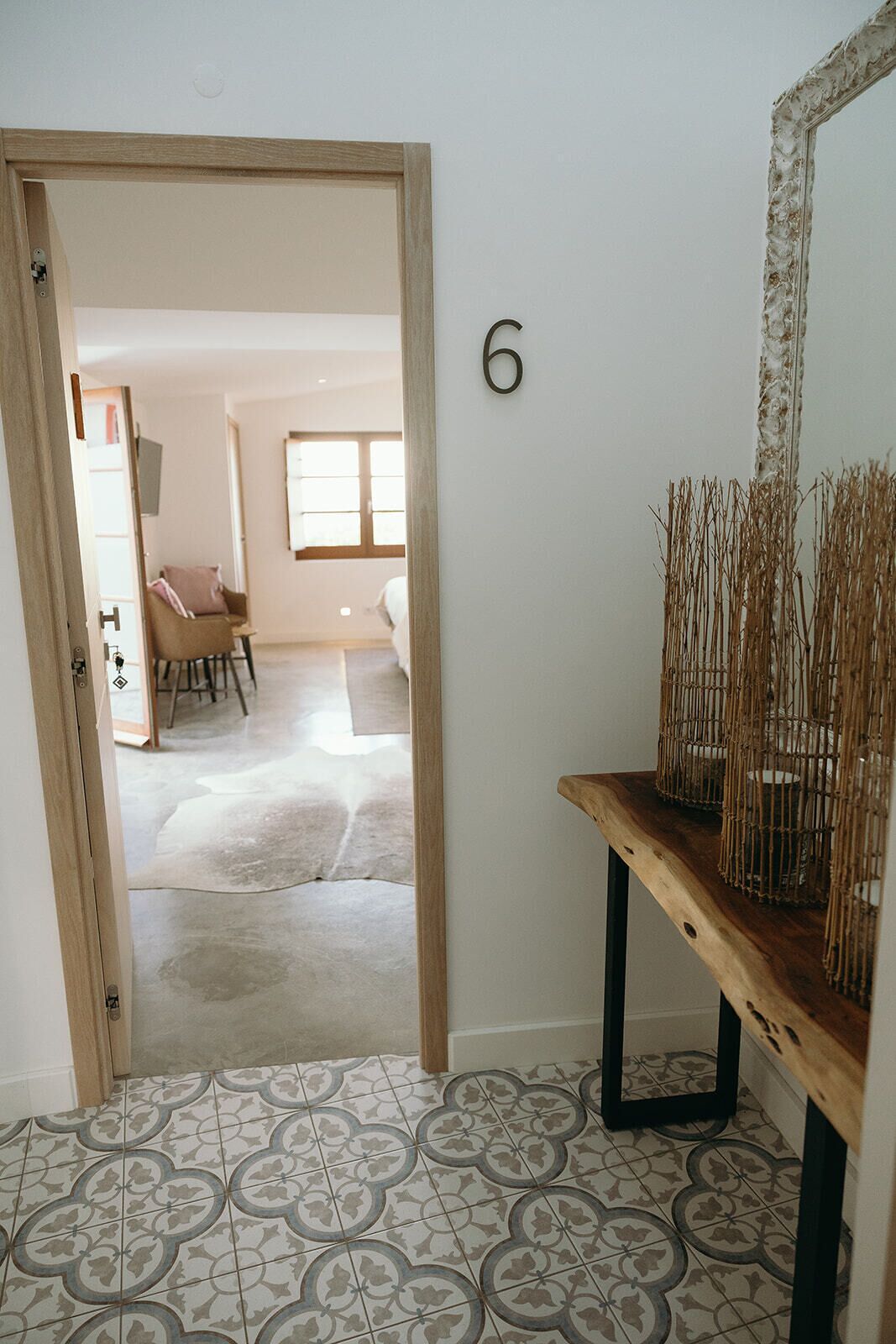Una habitación con puerta de madera, el número 6 en la pared, un espejo y una mesa con ramas decorativas.