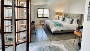 Un dormitorio con una cama grande, una mesita de noche, una silla y una ventana.