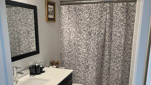 Un baño con un lavamanos blanco, armarios negros, un inodoro y una cortina de ducha estampada con motivos florales.