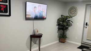 Una sala de estar con un televisor de pantalla plana montado en la pared, una planta en maceta, un reloj y una puerta.