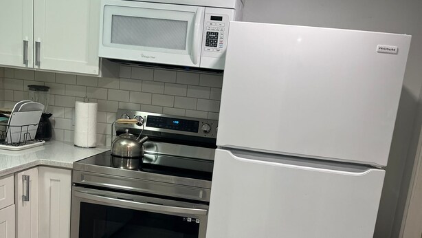 Una cocina con armarios blancos, horno de acero inoxidable, microondas y refrigerador.