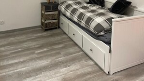 Een slaapkamer met een bed, nachtkastje, lamp, airconditioning en een raam met zonwering.