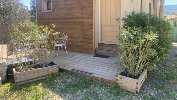 Een houten blokhut met een houten terras, een deur en een klein raam.