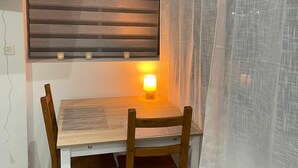 Een eetgedeelte met een houten tafel en stoelen, een lamp en een raam met jaloezieën.