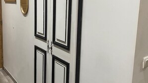 Een gang met een dubbele deur, een klein raam en twee houten decoraties aan de muur.
