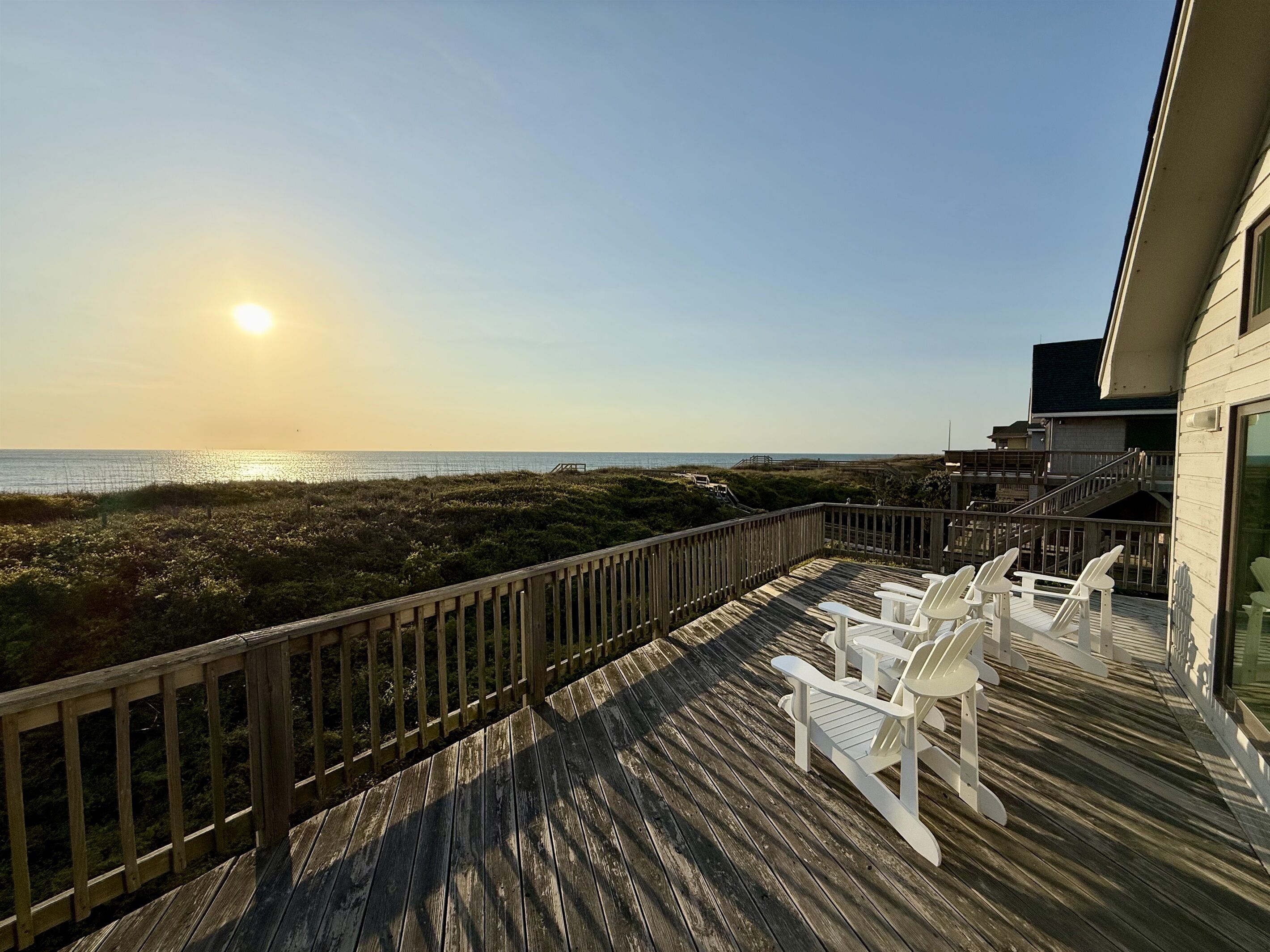 A wooden deck with white chairs overlooking a beach.