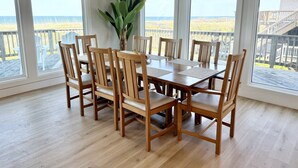 Un espace repas avec une table et des chaises en bois, de grandes fenêtres et une vue sur la plage.