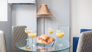 Ein Essbereich mit einem Glastisch, zwei Stühlen, einer Lampe und einem Teller mit Croissants und Orangensaft.