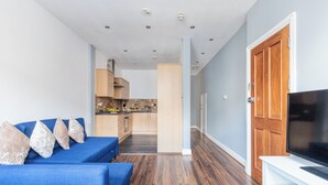 Ein modernes Wohnzimmer mit einem blauen Sofa, Holzböden und einem Fernseher auf einem weißen Lowboard.