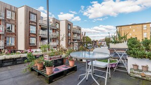 Eine Dachterrasse mit rundem Tisch und Stühlen, umgeben von Topfpflanzen und einer kleinen Sitzecke.