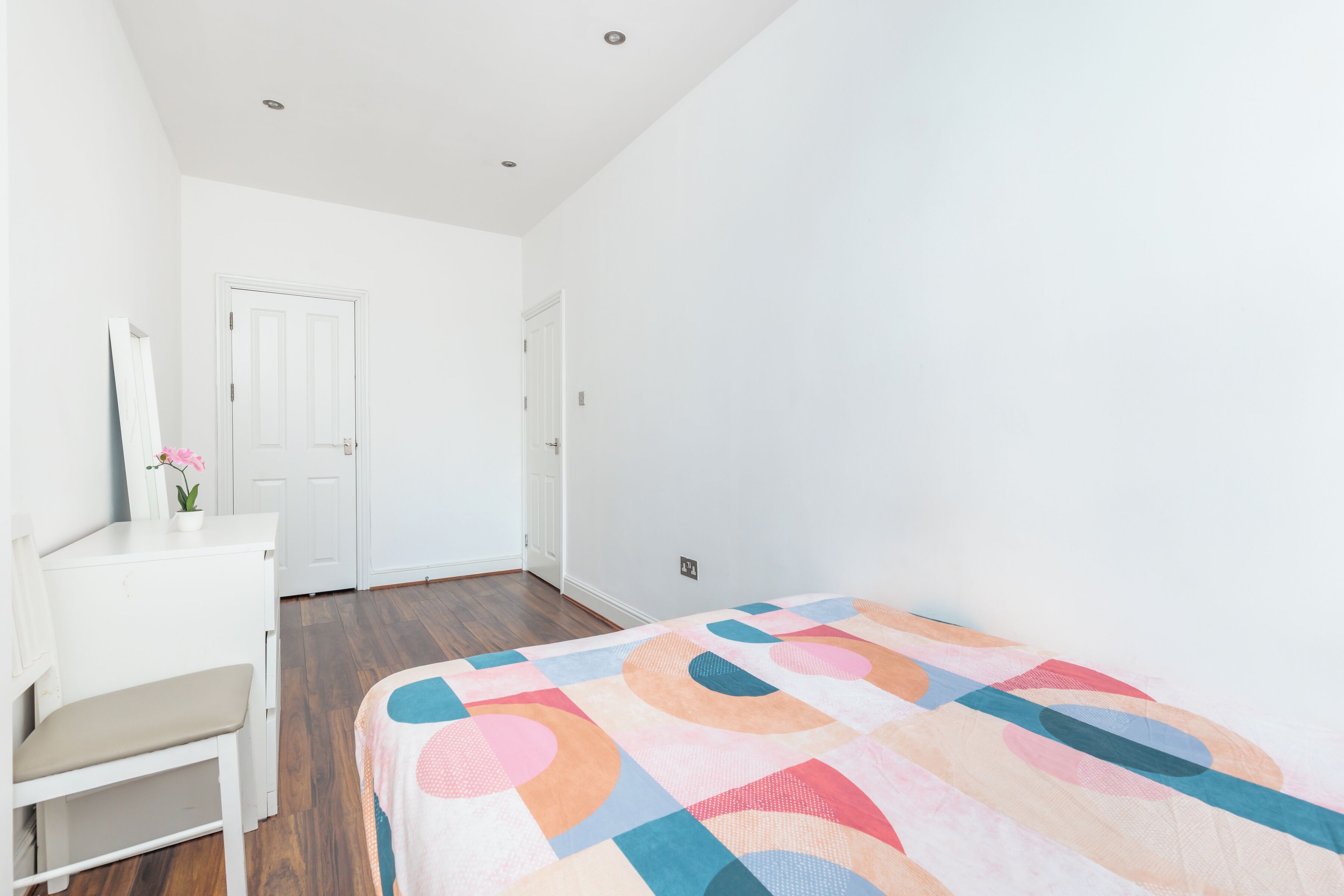 Una camera da letto con un letto, una scrivania e una sedia. Si vede una porta e una finestra.