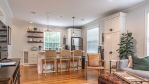 A modern kitchen with wooden cabinets, a dining area with chairs, a leather sofa, and a large plant. - The McCaskill Cottage in the Village of Pinehurst!  (Pinehurst)