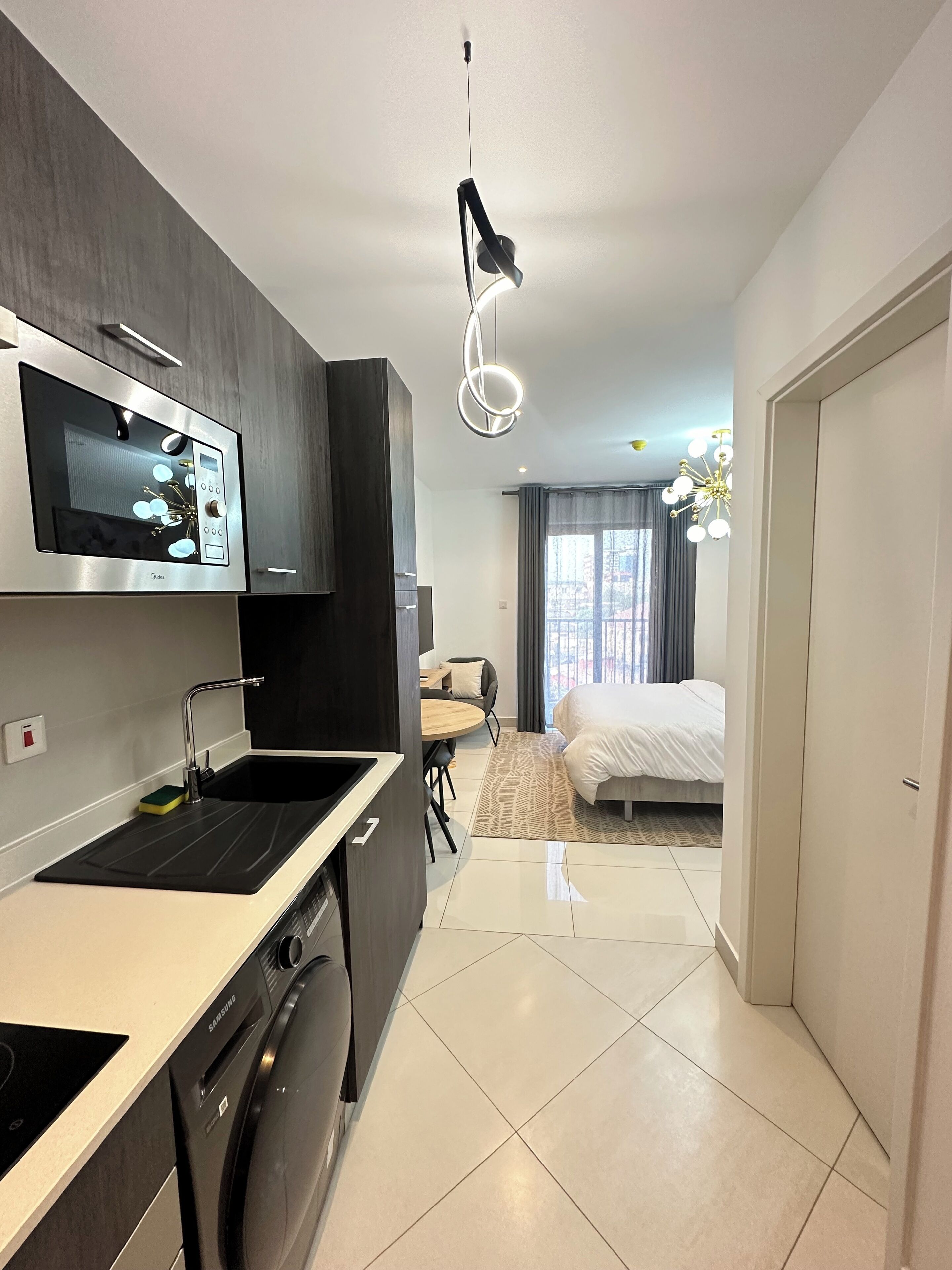 A modern kitchen with a built-in microwave, a Samsung washing machine, and a dining area with a table and chairs.