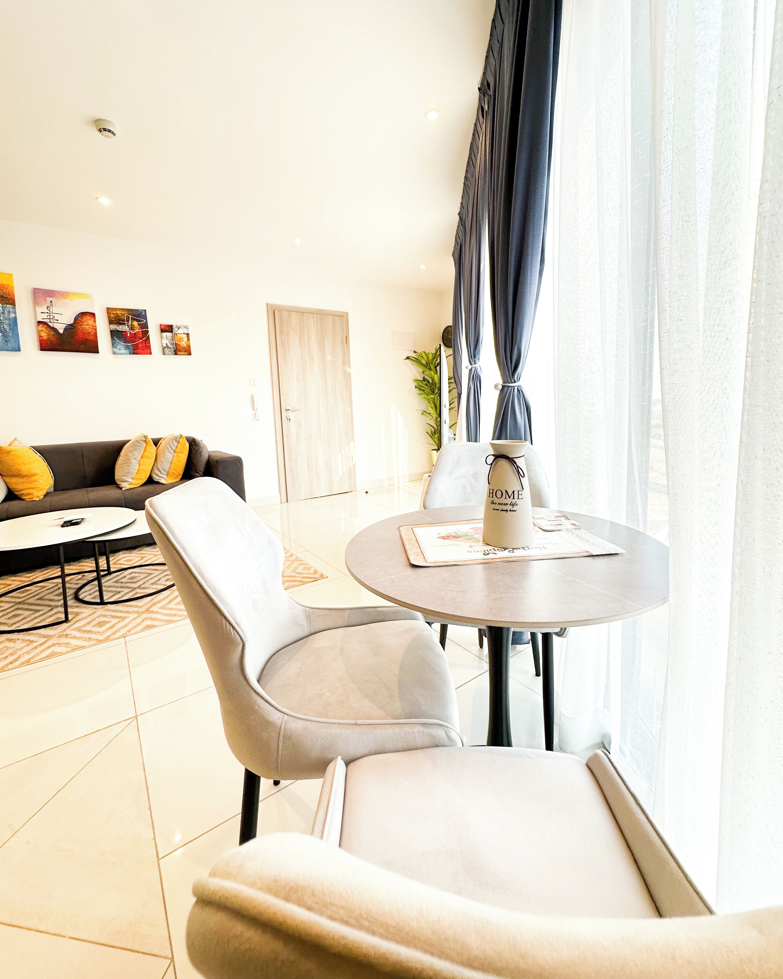 Un salon moderne avec un canapé, une table ronde et une table basse. Il y a des tableaux accrochés au mur et une plante dans un coin.