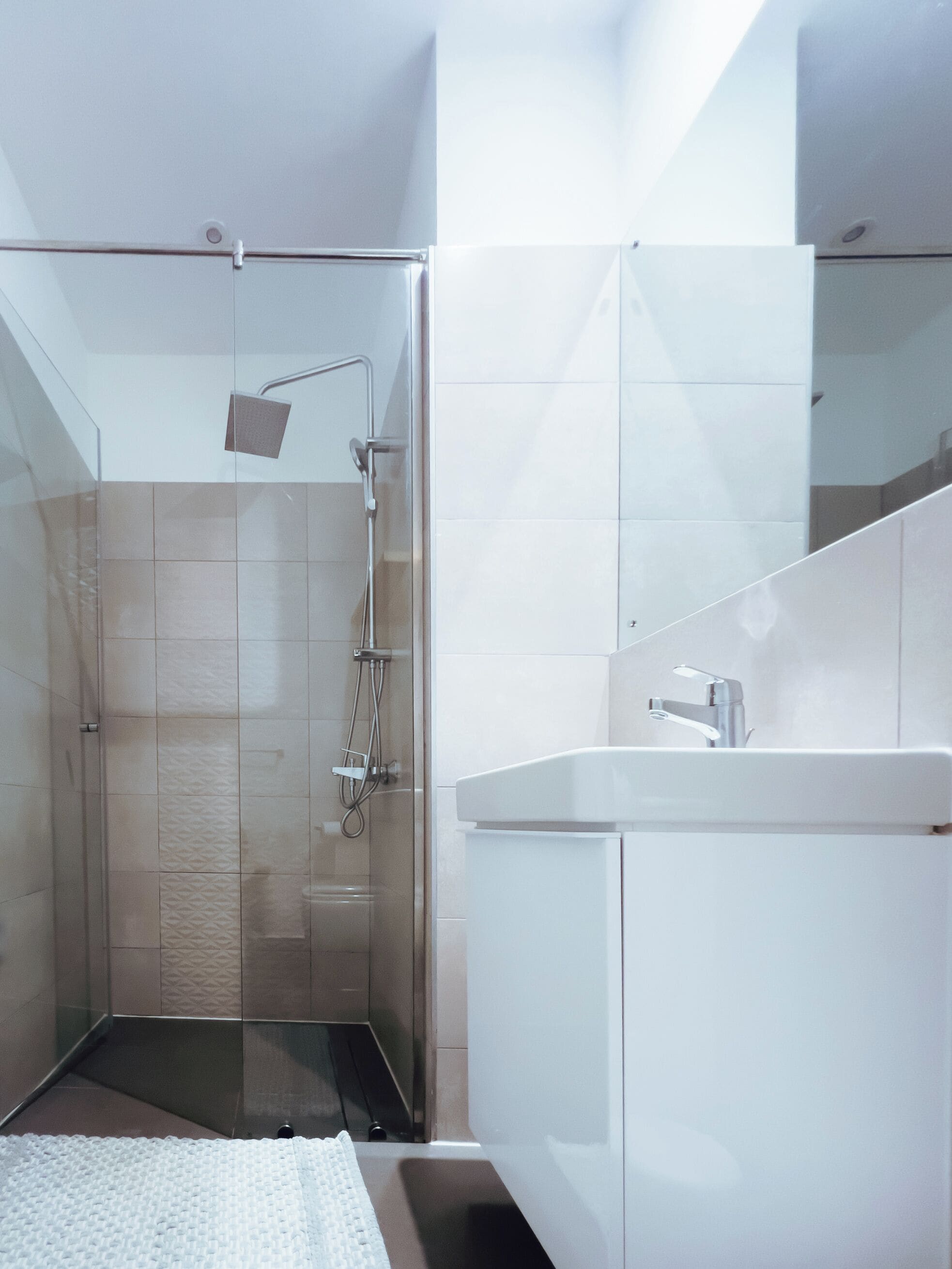 Un baño moderno con ducha envuelta en vidrio, lavamanos blanco y espejo grande.