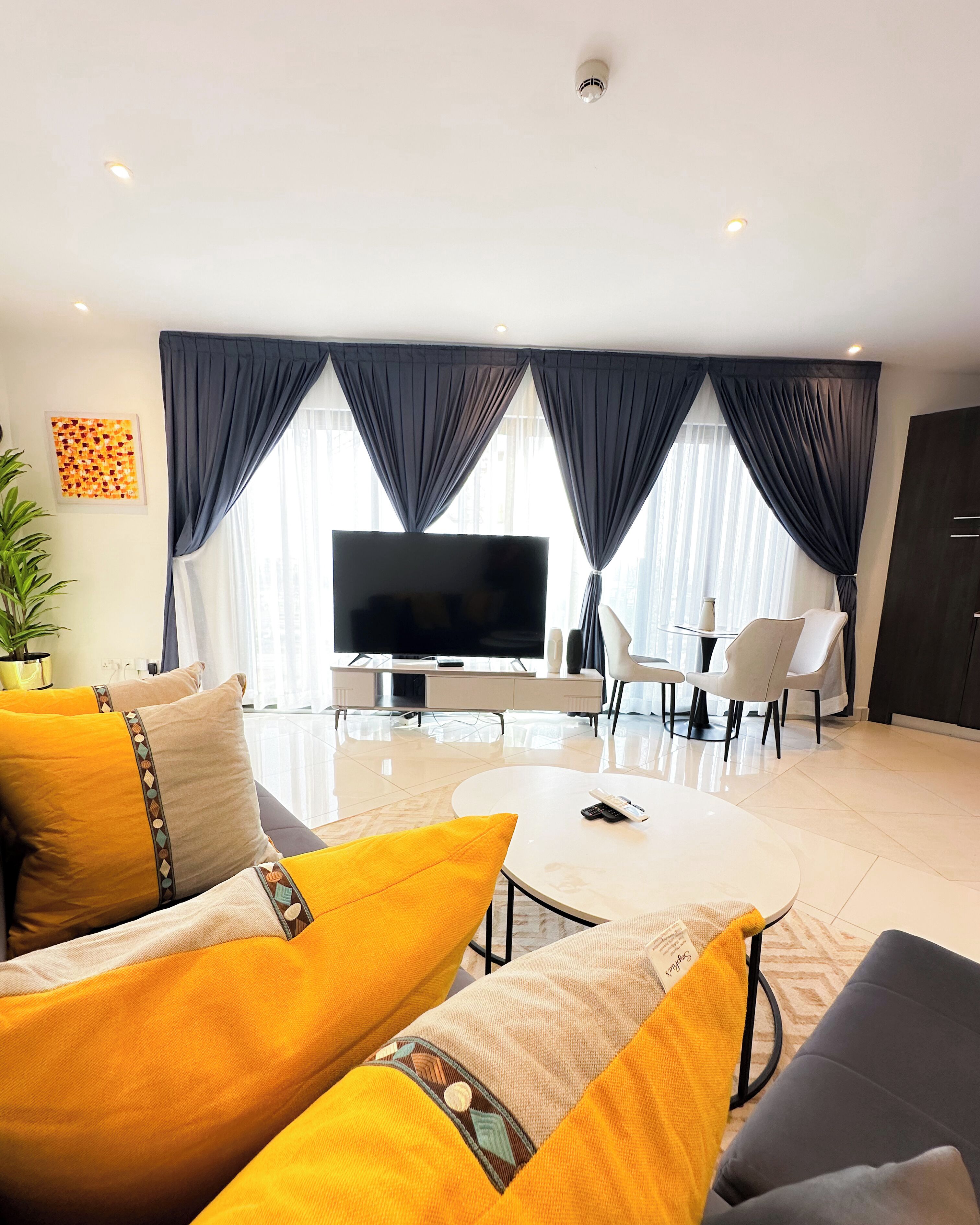 A modern living room with a flat-screen TV, a coffee table, and a dining area with chairs and a small table.