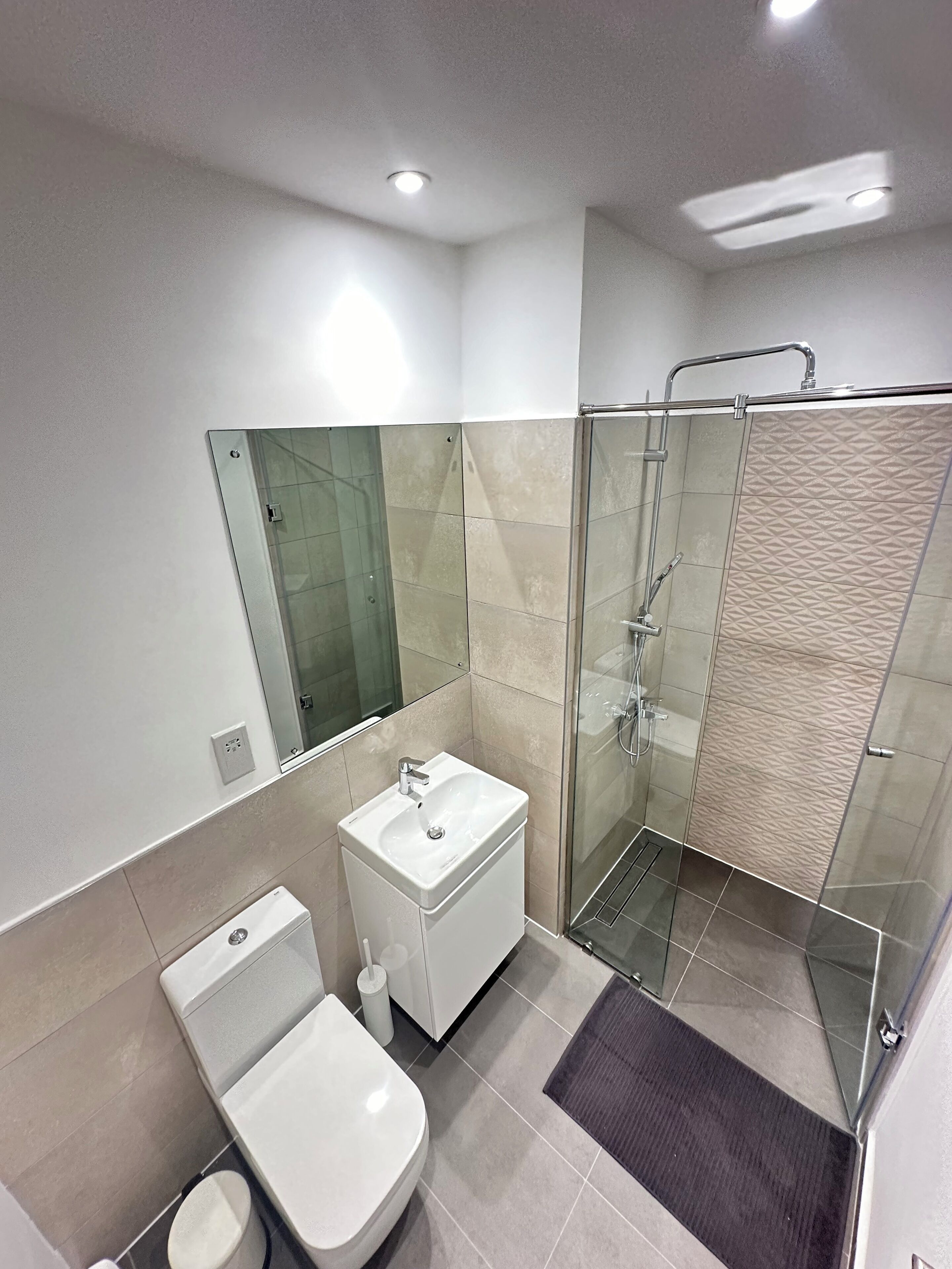 A modern bathroom with a glass-enclosed shower, a white sink, and a toilet.