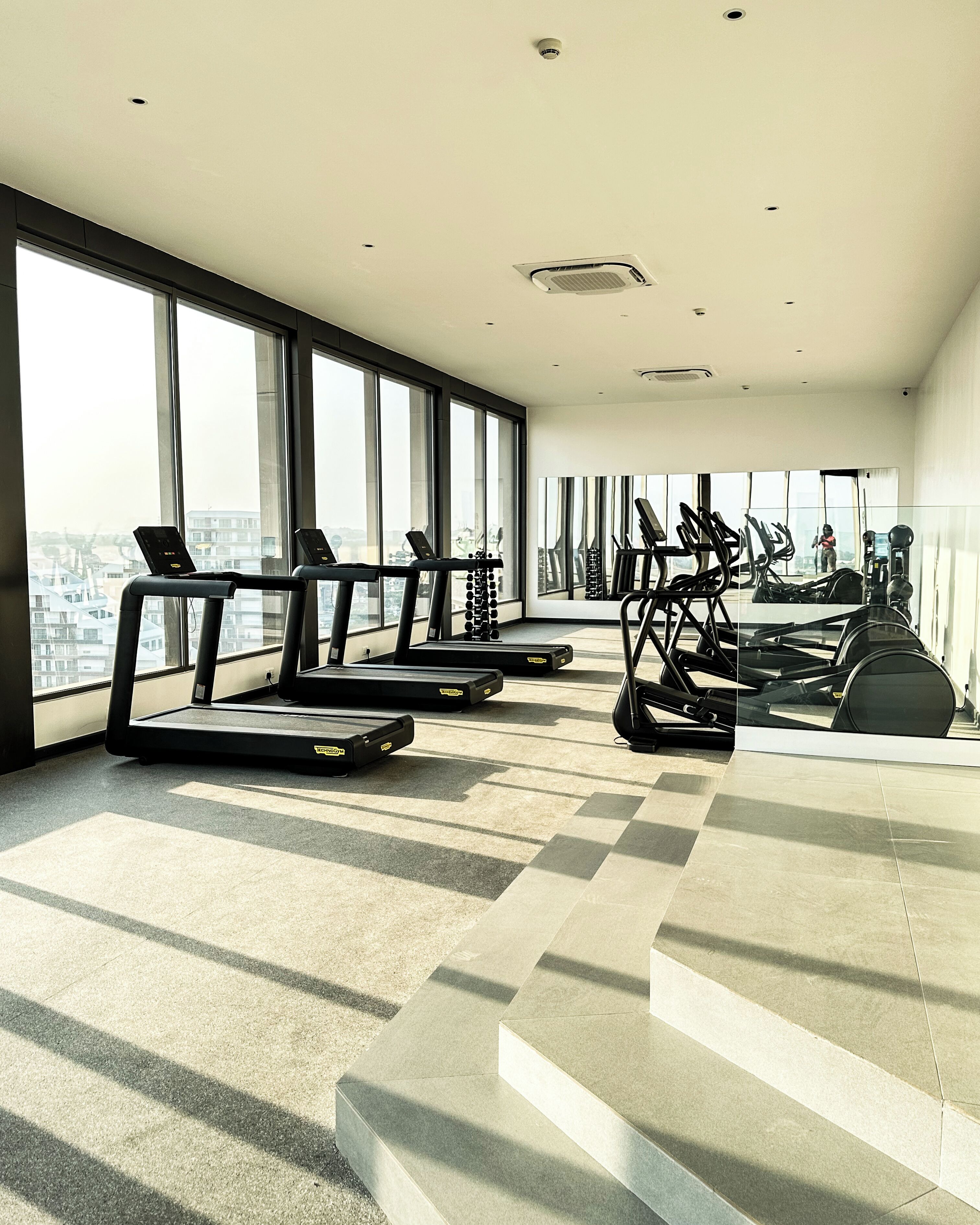 A modern gym with treadmills, elliptical machines, and a large mirror.