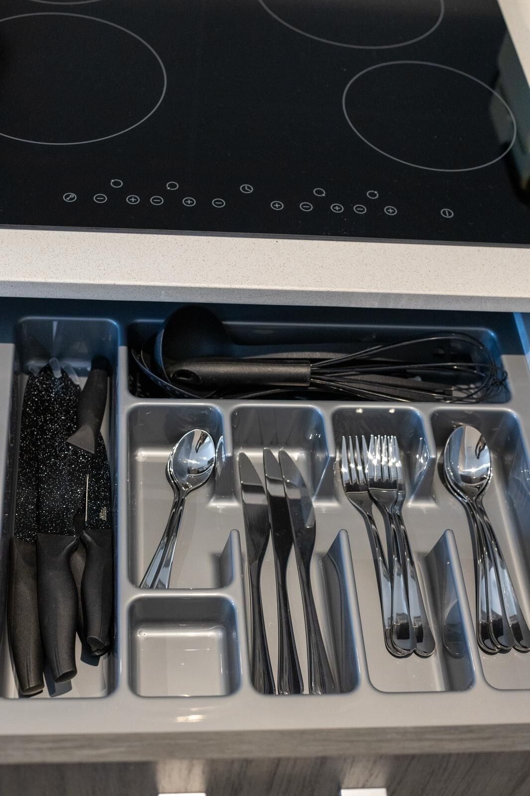 Un cajón con utensilios de cocina, como cucharas, tenedores, cuchillos y un batidor.