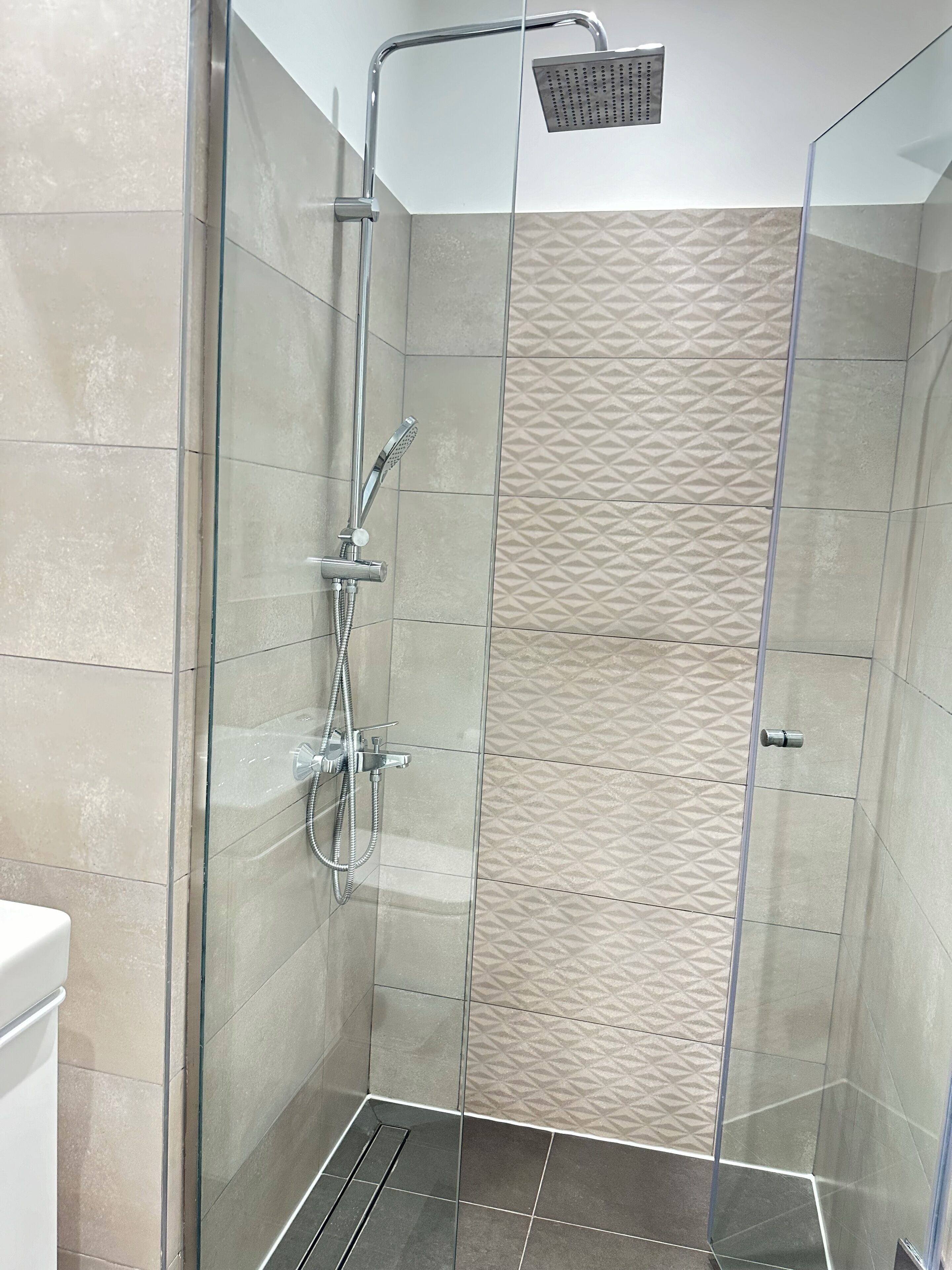 Una ducha con cerramiento de vidrio, con cabezal de ducha de mano y otro cabezal de lluvia montado en la pared.