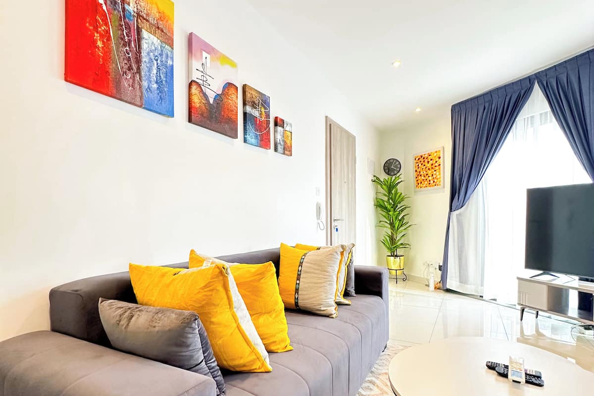 A modern living room with a grey sofa, yellow and grey cushions, a round coffee table, and a flat-screen TV.