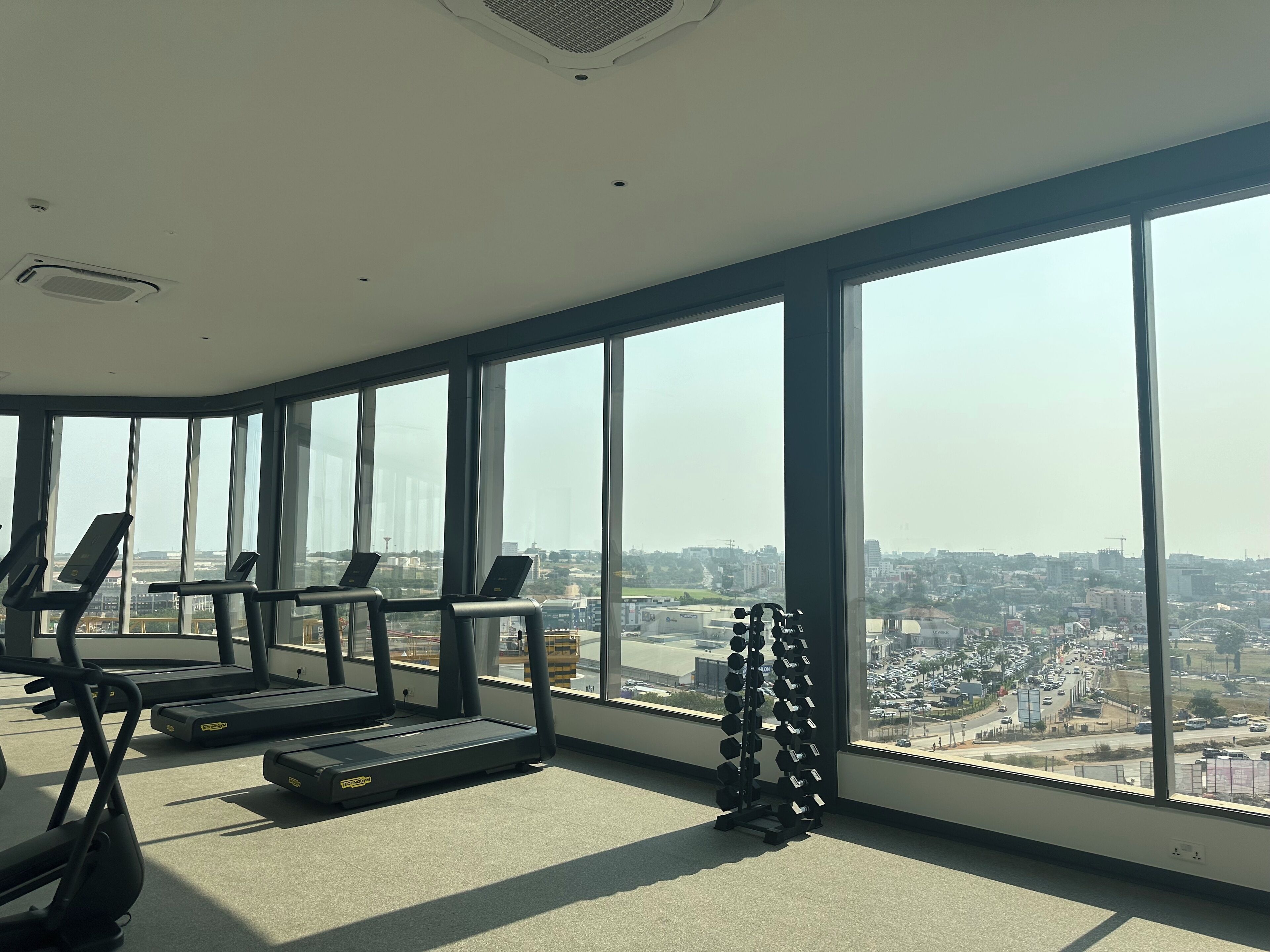 A gym with treadmills and a dumbbell rack, large windows, and a city view.