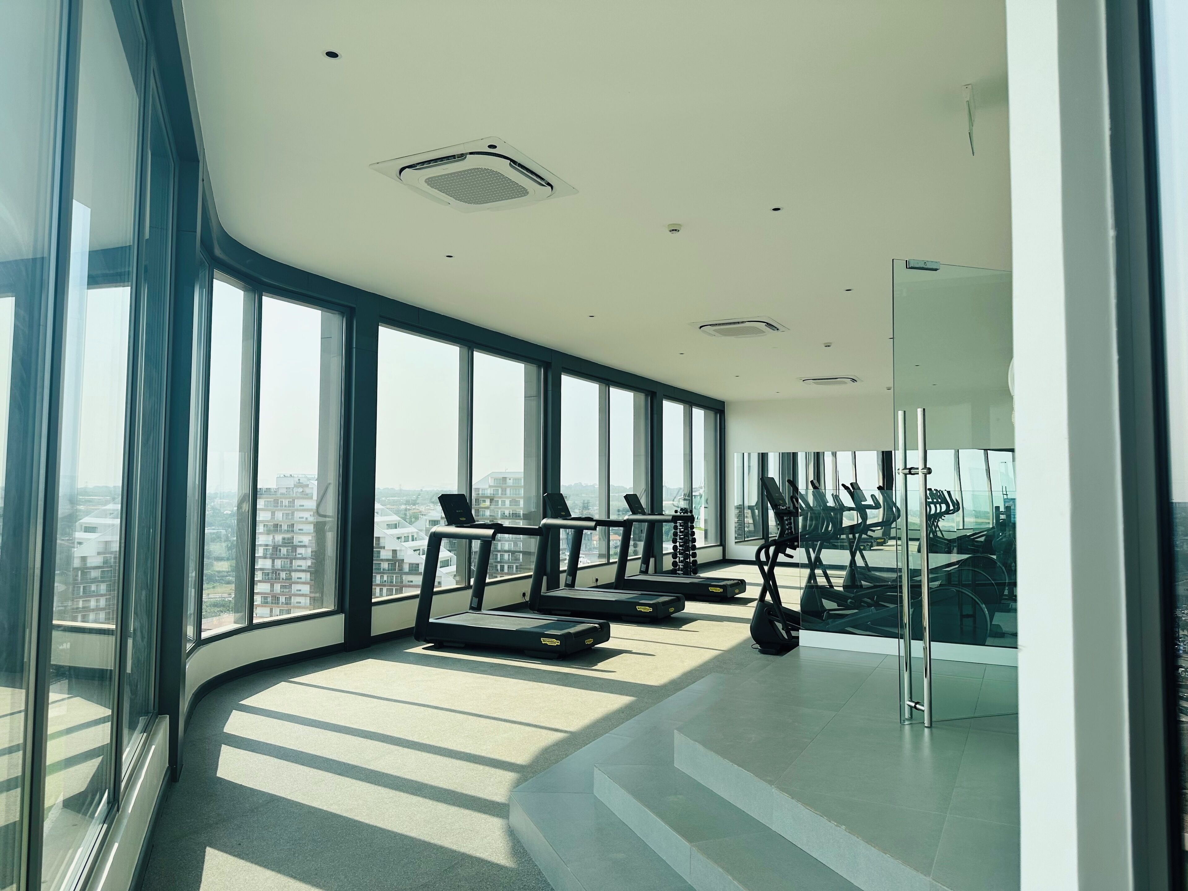 Un gimnasio moderno con amplios ventanales, cintas de correr y equipo de ejercicio.