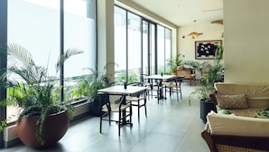 A spacious indoor area with large windows, multiple seating arrangements, and potted plants. - Loxwood Apartment (Accra)