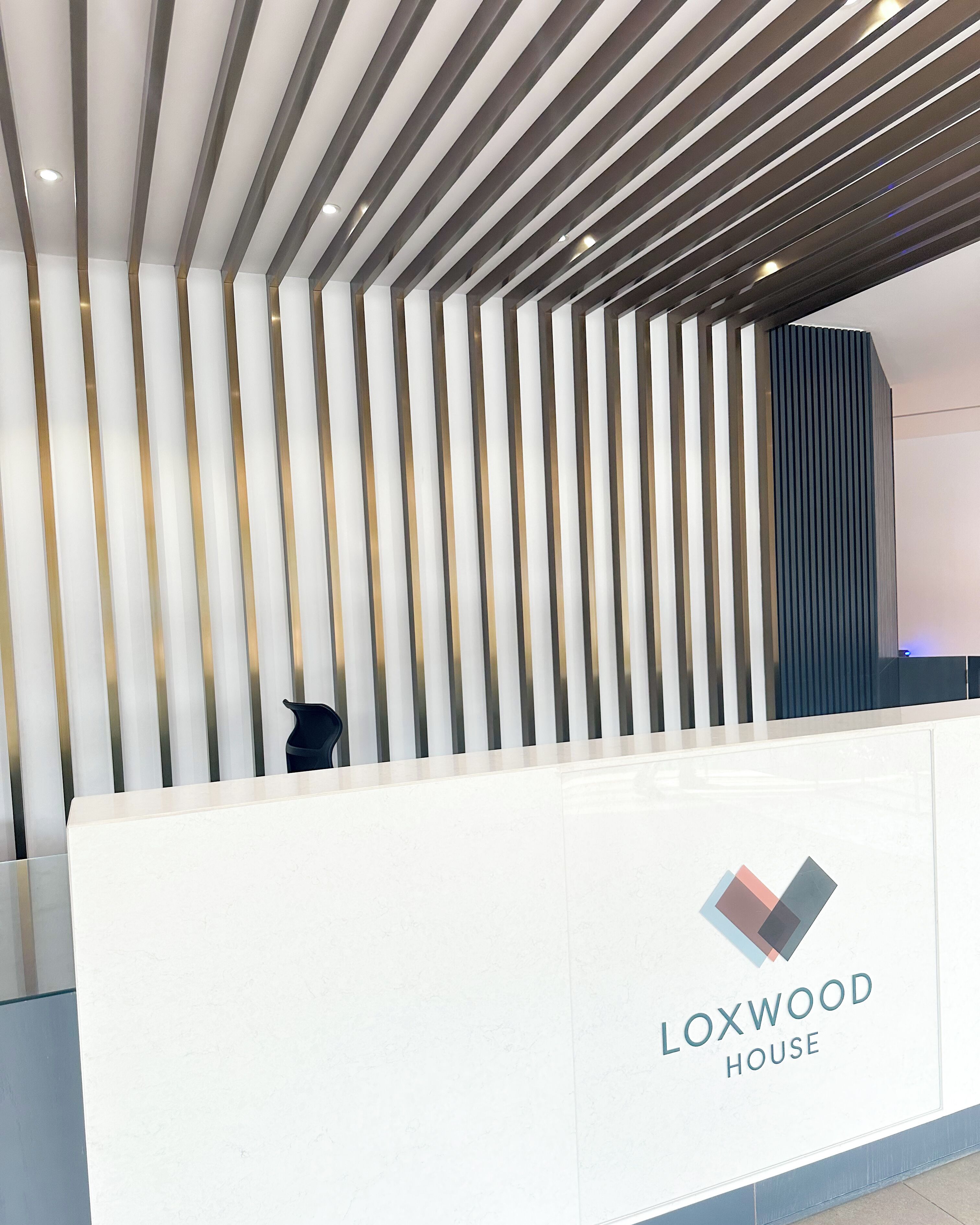 A reception desk with a modern design, featuring vertical slats and a logo for Loxwood House.