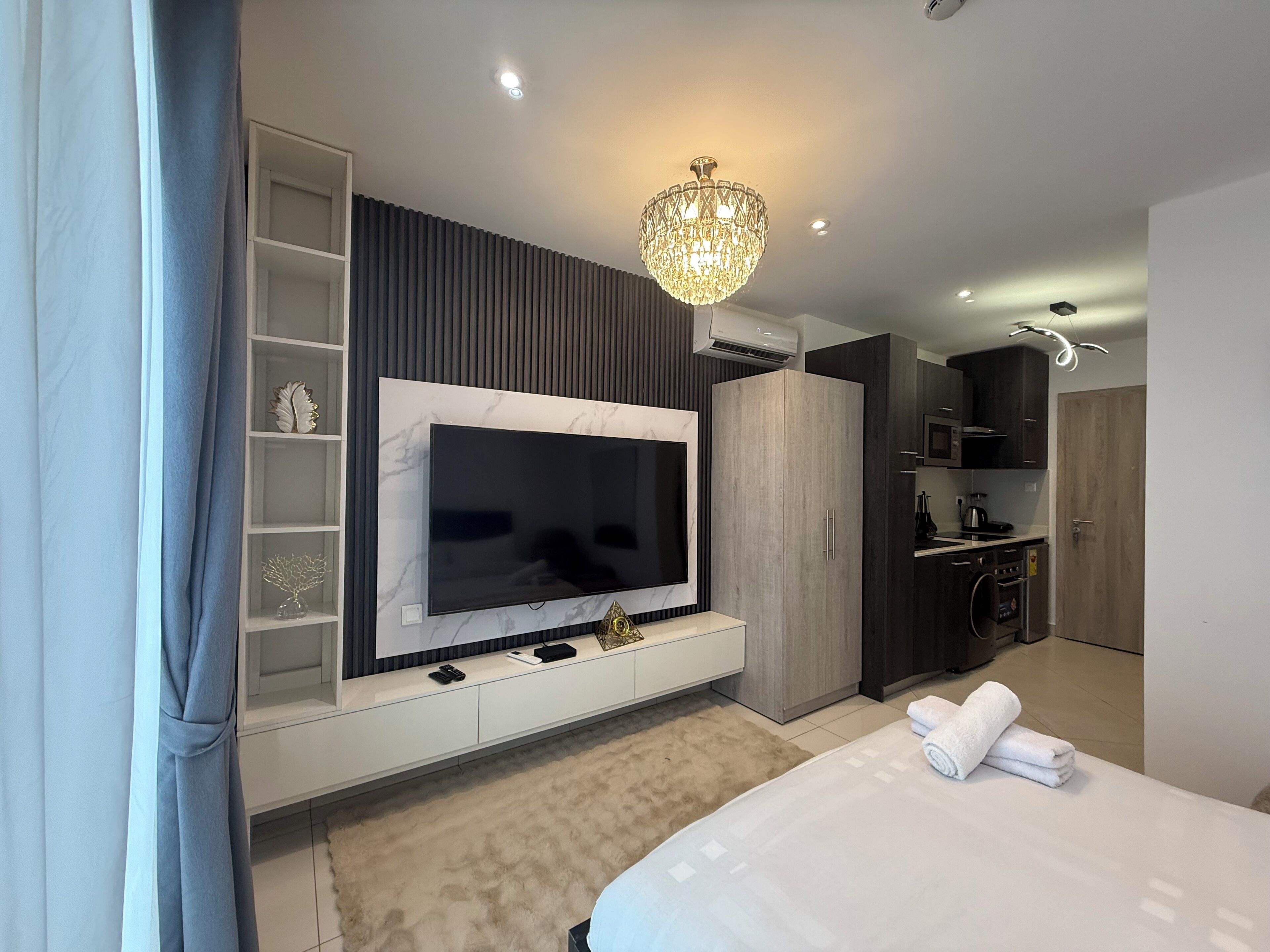 Um quarto moderno com uma cama grande, uma TV na parede, um guarda-roupa e uma kitchenette.