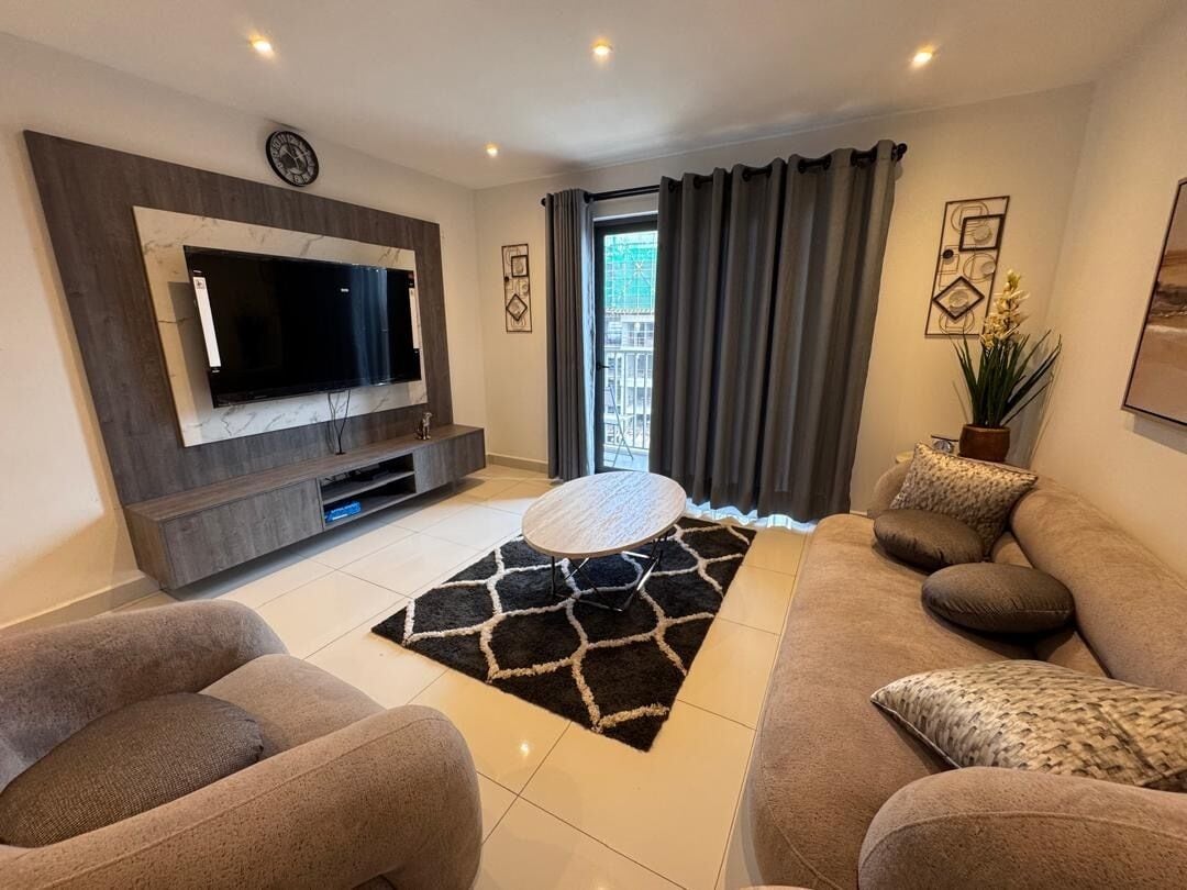 A modern living room with a large flat-screen TV, a round coffee table, and two sofas.