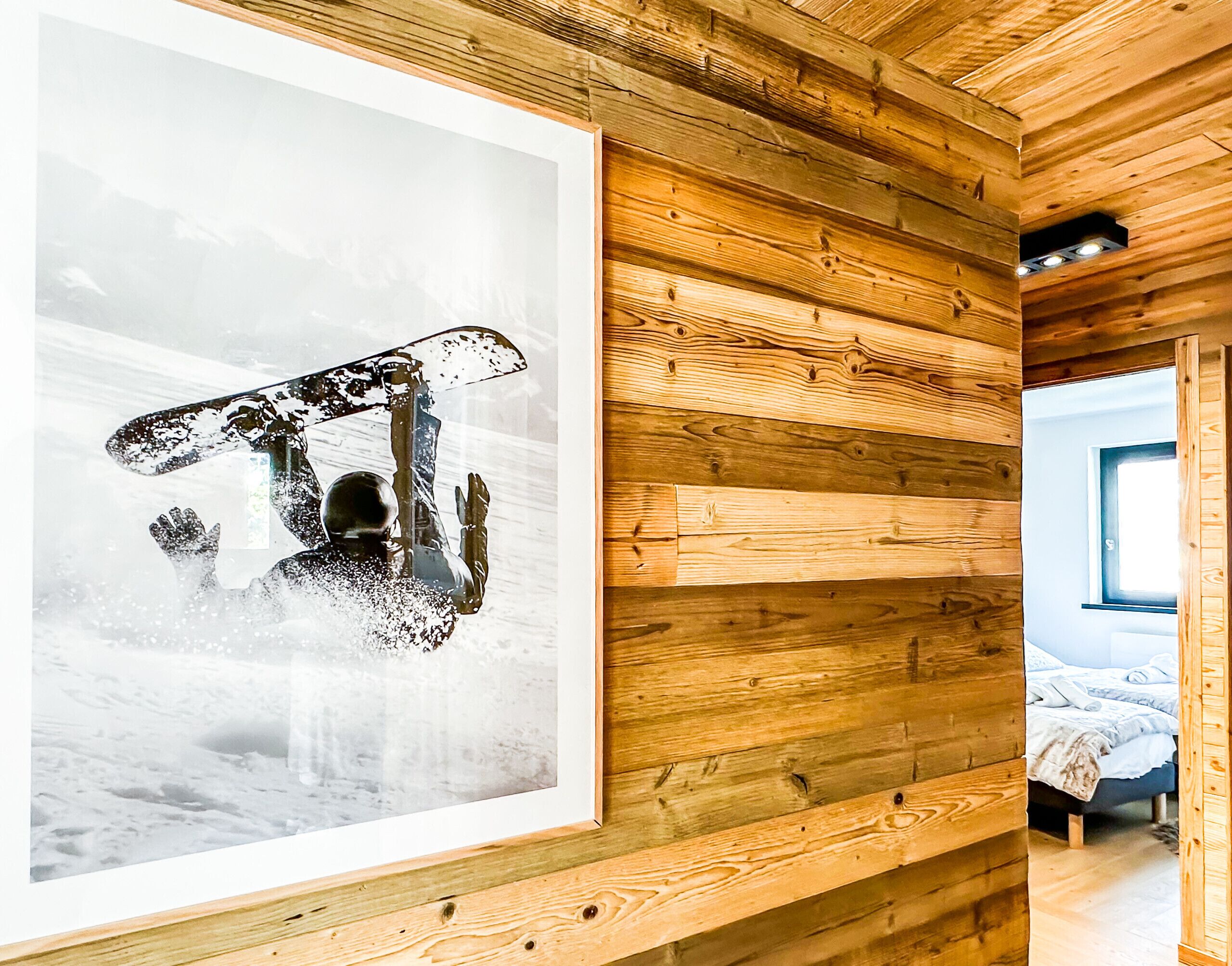 A wooden cabin interior with a framed photograph on the wall, a bed, and a window.