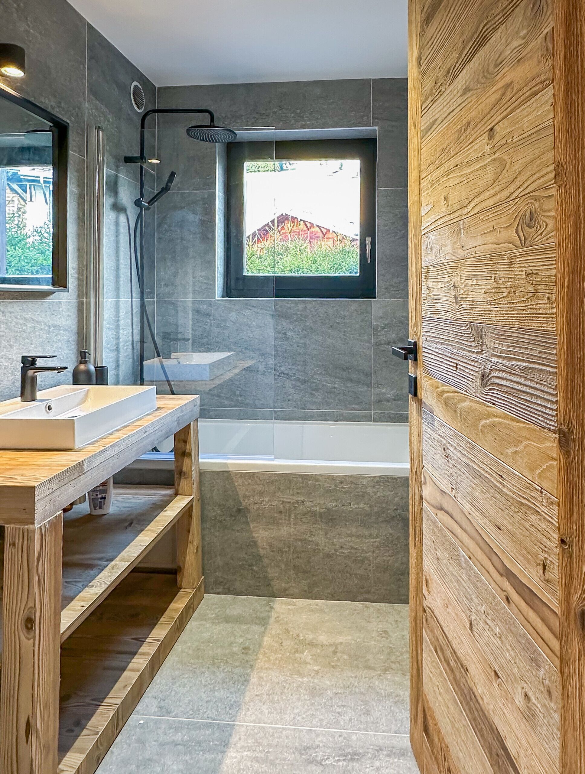 Une salle de bain moderne avec un meuble-lavabo en bois, une baignoire et une fenêtre donnant sur un paysage verdoyant.