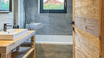 Une salle de bain moderne avec un meuble-lavabo en bois, une baignoire et une fenêtre donnant sur un paysage verdoyant.